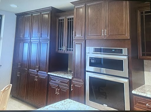 Kitchen with dark wood cabinets, built-in double oven, and granite countertop