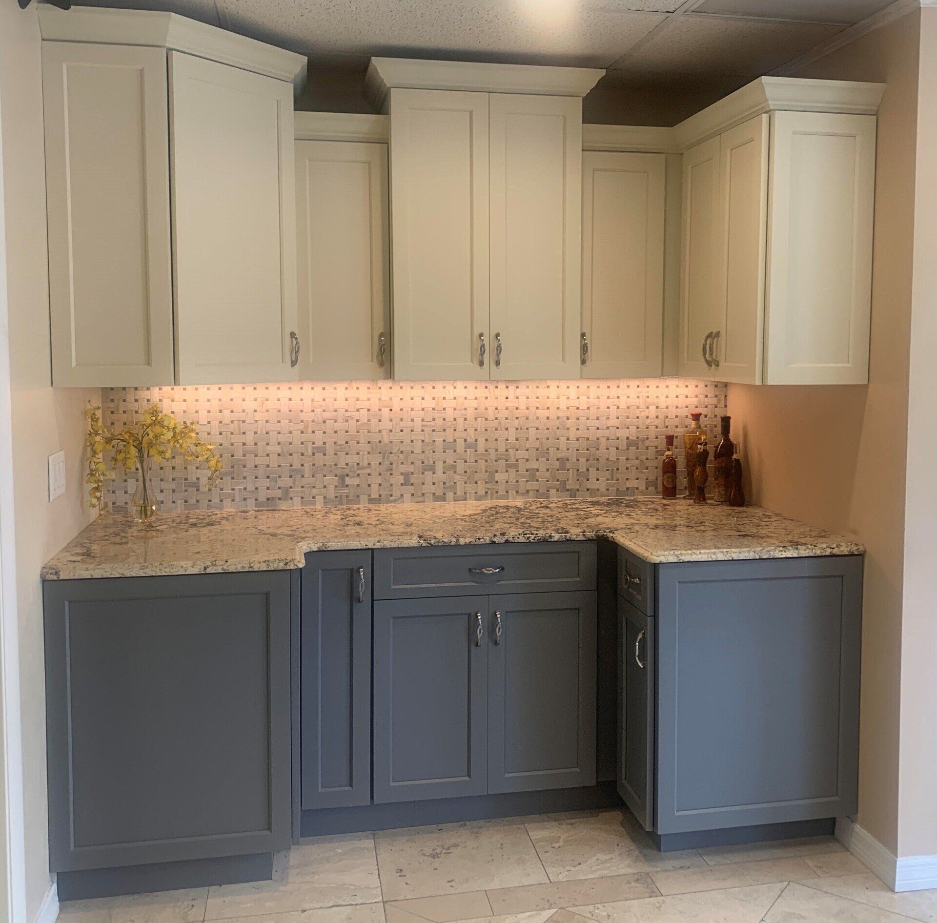 Kitchen with white upper cabinets, gray lower cabinets, and mosaic tile backsplash under warm under-cabinet lighting
