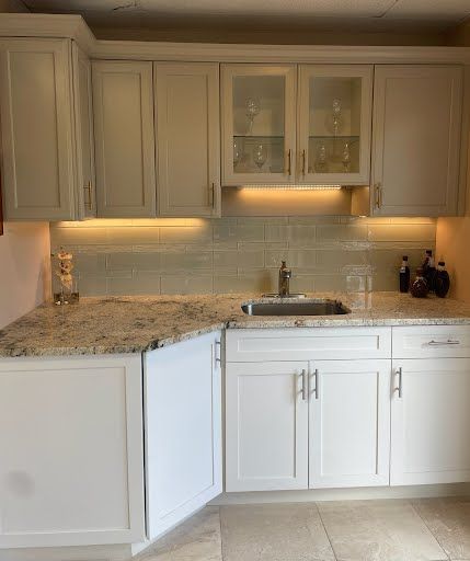White kitchen with granite countertops, glass-front cabinets, under-cabinet lighting, and a stainless sink.
