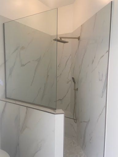 Walk-in shower with marble-look tile walls, glass partition, and chrome showerhead