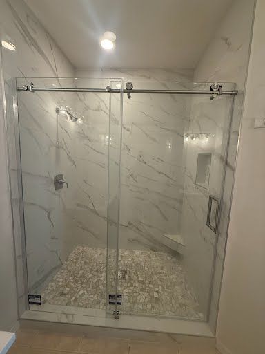 Modern shower with marble tile walls and pebble floor, enclosed by clear sliding glass doors.