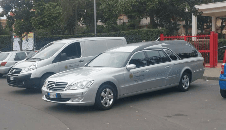 Una station wagon argentata e un furgone bianco parcheggiati in una strada vicino a una recinzione rossa.