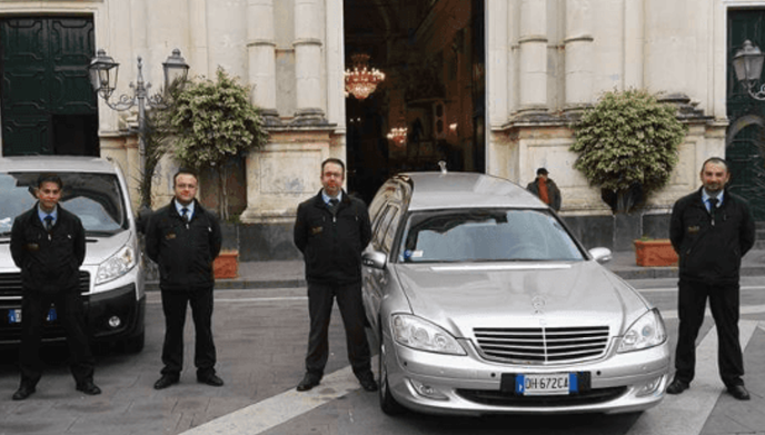 Funzionari in piedi accanto a due auto parcheggiate all'esterno dell'ingresso principale di un edificio.