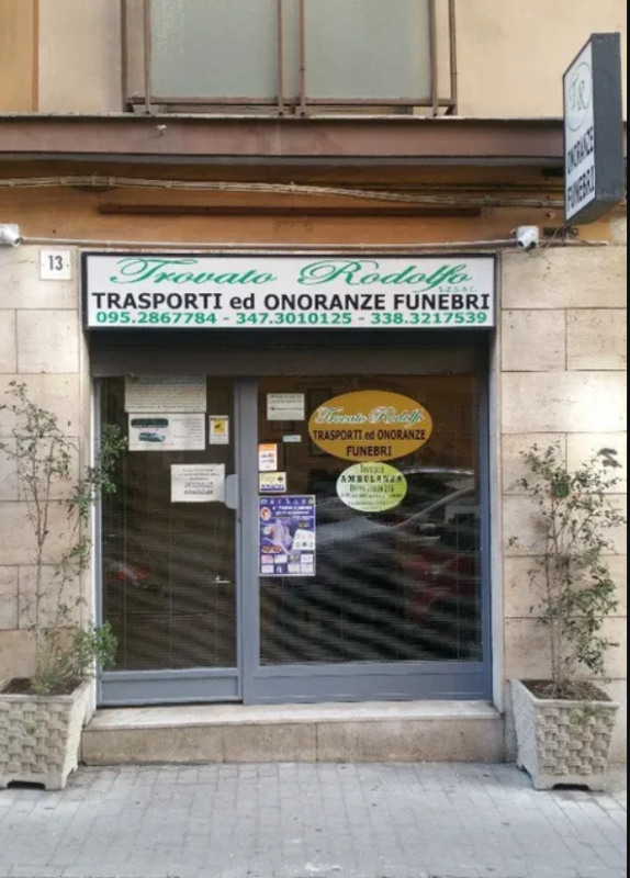 Vetrina di un'impresa di servizi funebri con ingresso in vetro e insegna verde sopra.