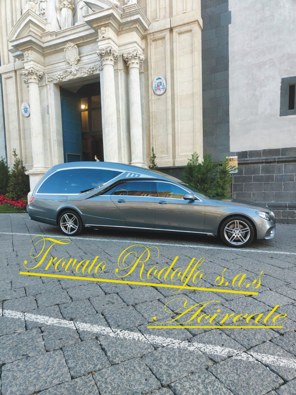 Una station wagon Mercedes color argento parcheggiata davanti a un edificio decorato con una scritta gialla sovrapposta.