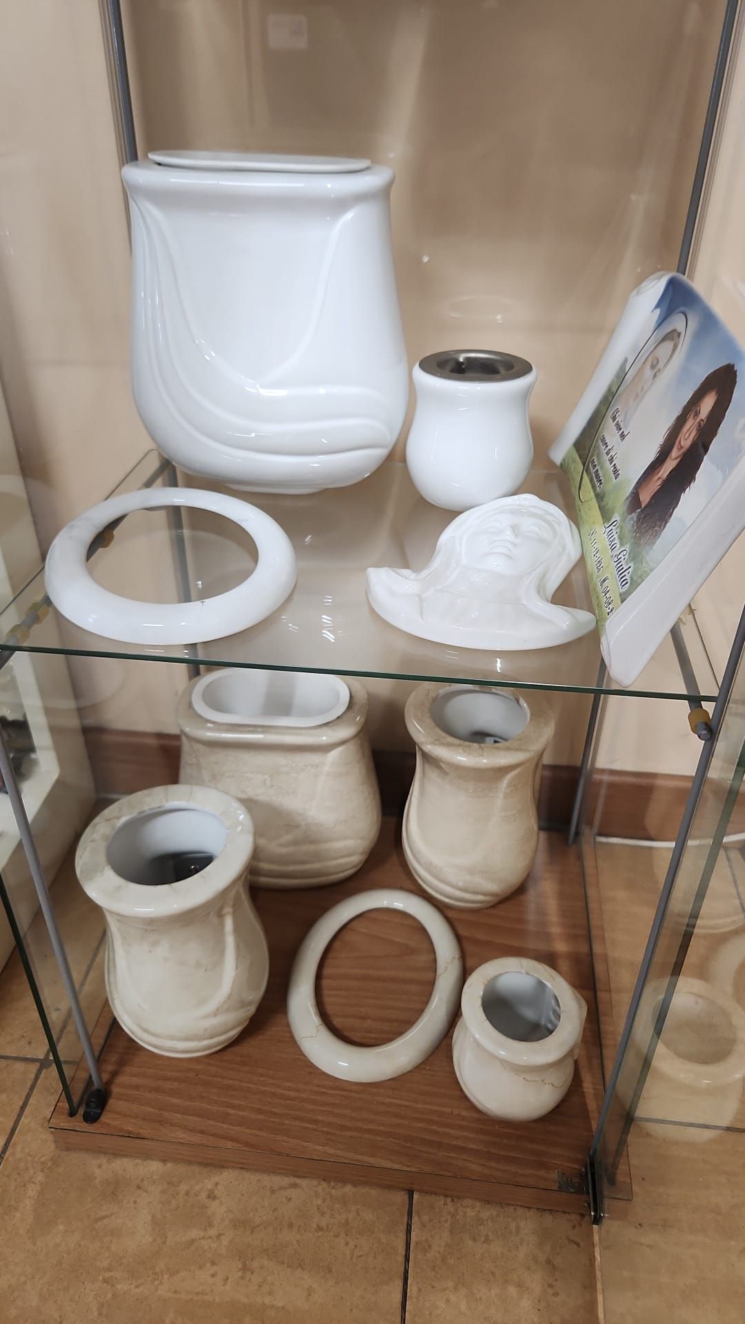 Vetrina con assortimento di sanitari e rubinetteria in ceramica bianca per WC e lavabo e una piccola foto incorniciata.