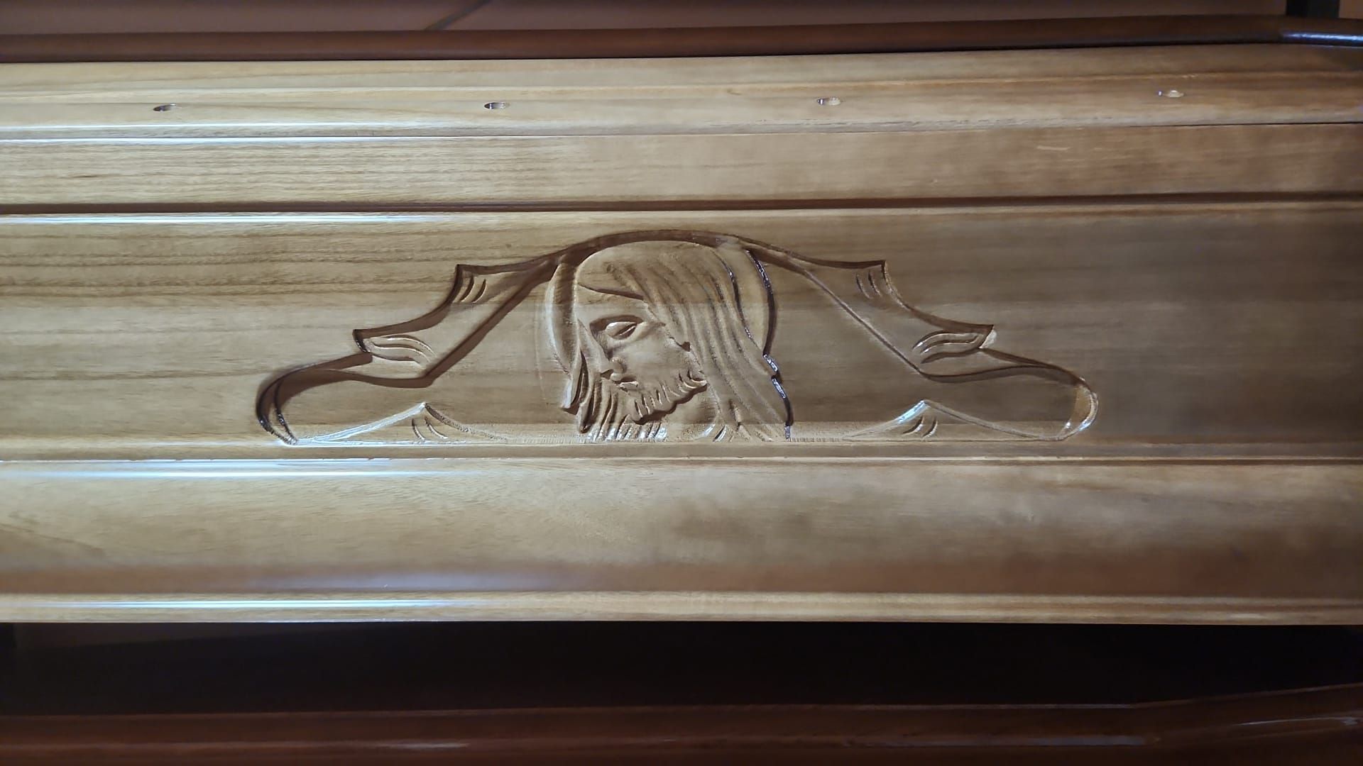 Coperchio di bara in legno con un ritratto religioso inciso al centro e intagli decorativi sui lati.