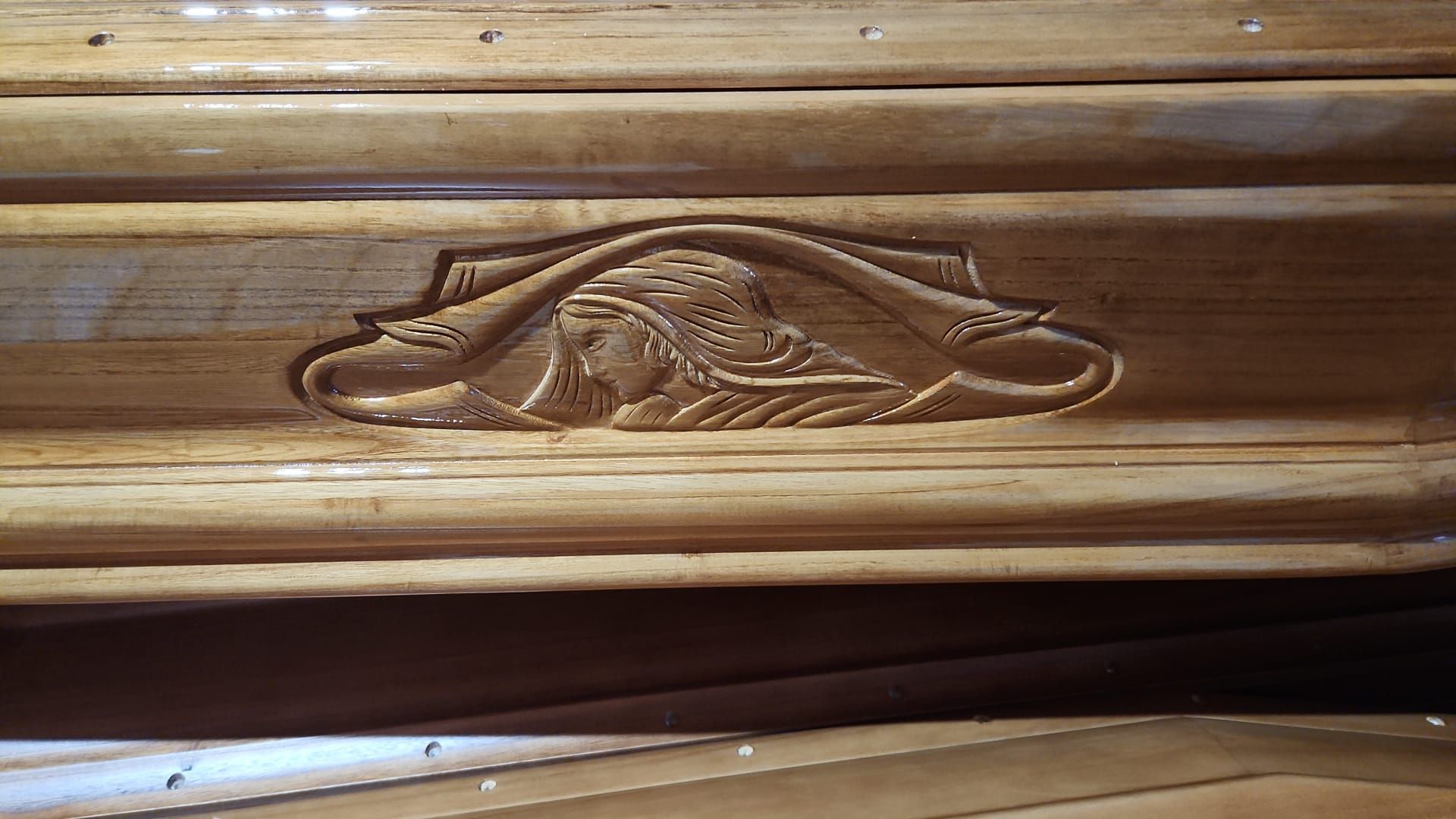 Primo piano di un medaglione floreale in legno intagliato su un pannello di legno marrone.