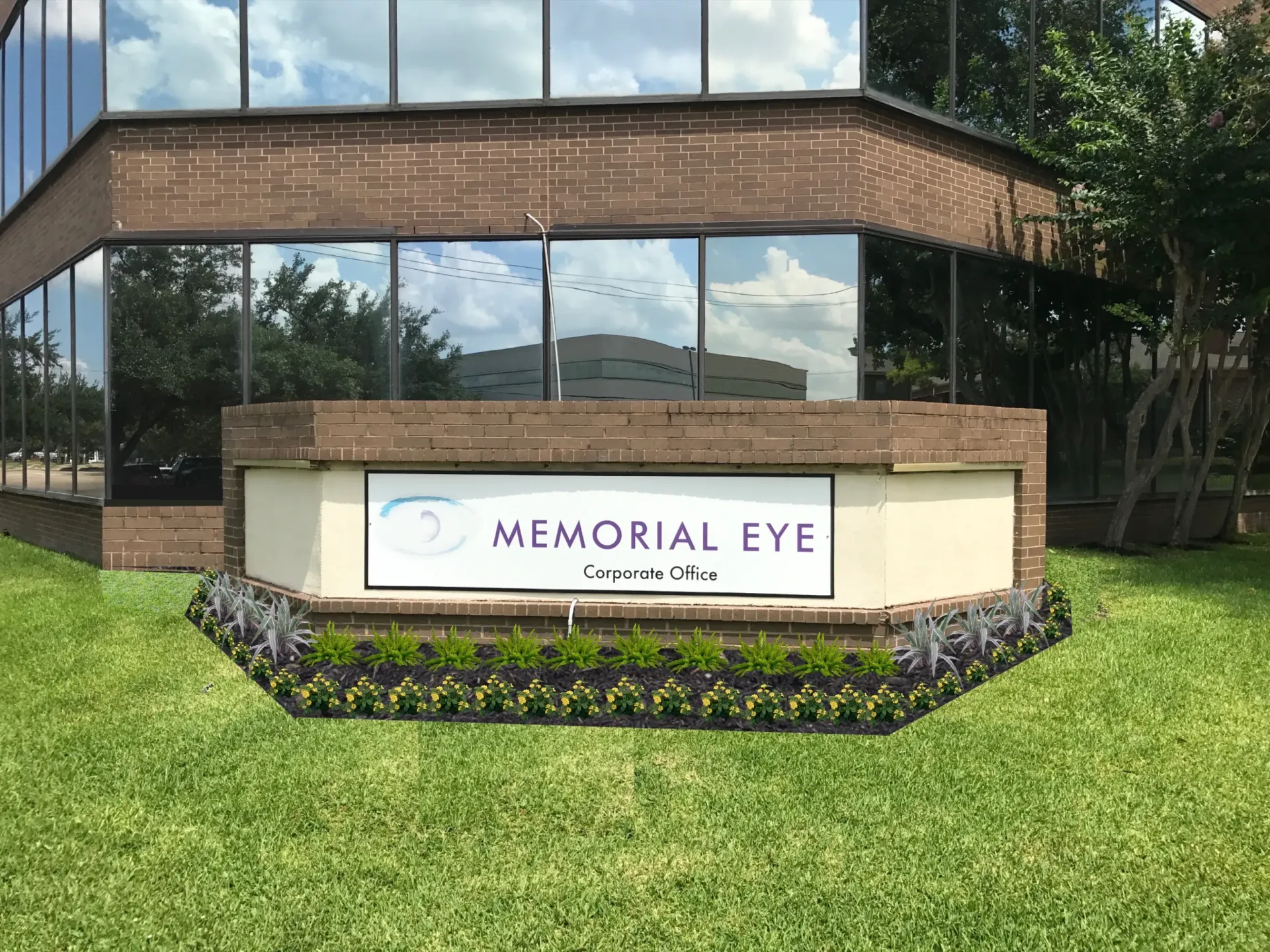 Memorial Eye Clinic sign in front of a brick-and-glass building, with lawn and flowers