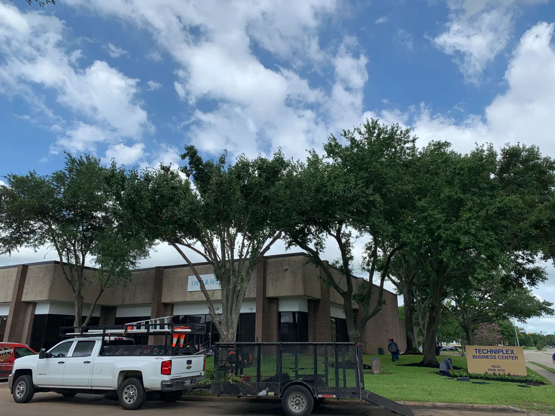 Parking lot with white pickup trucks, trees, and a low building under a partly cloudy sky
