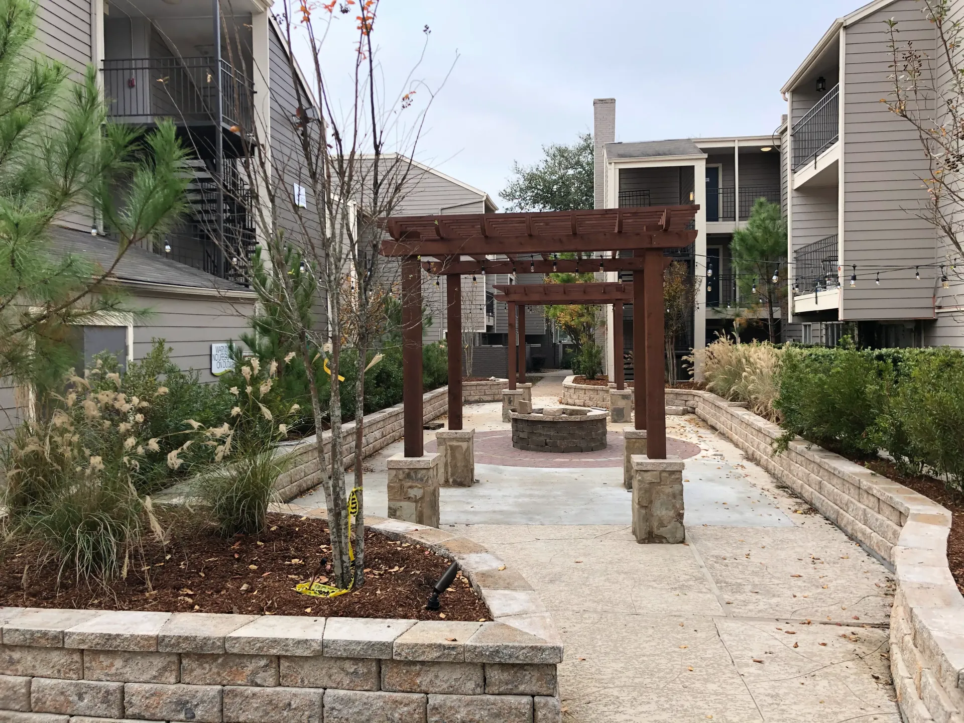 Modern apartment courtyard with a wooden pergola over a gravel path and landscaped planters