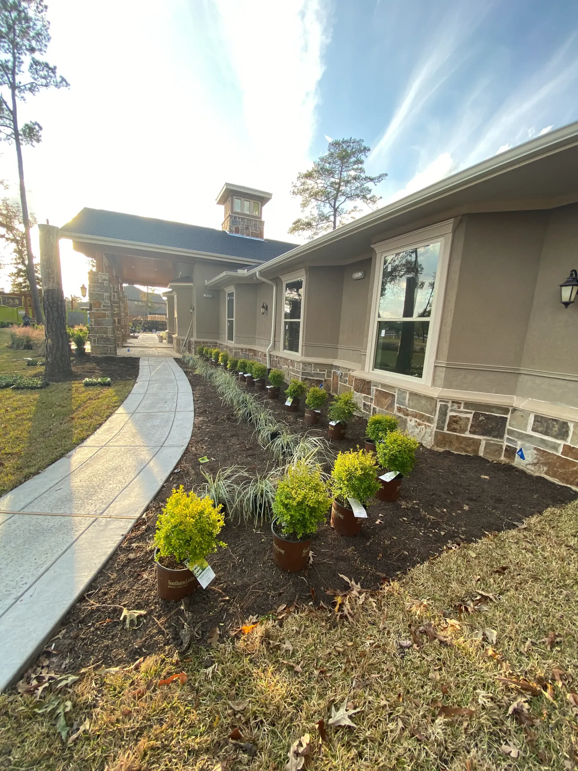 Landscaped front walkway with yellow flowers beside a stone house under a covered porch