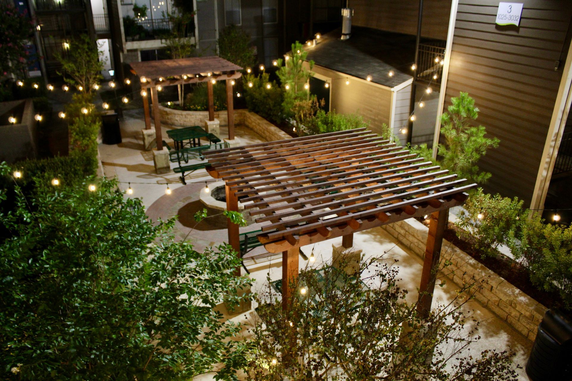 Night-lit backyard patio with pergola, string lights, seating, and plants