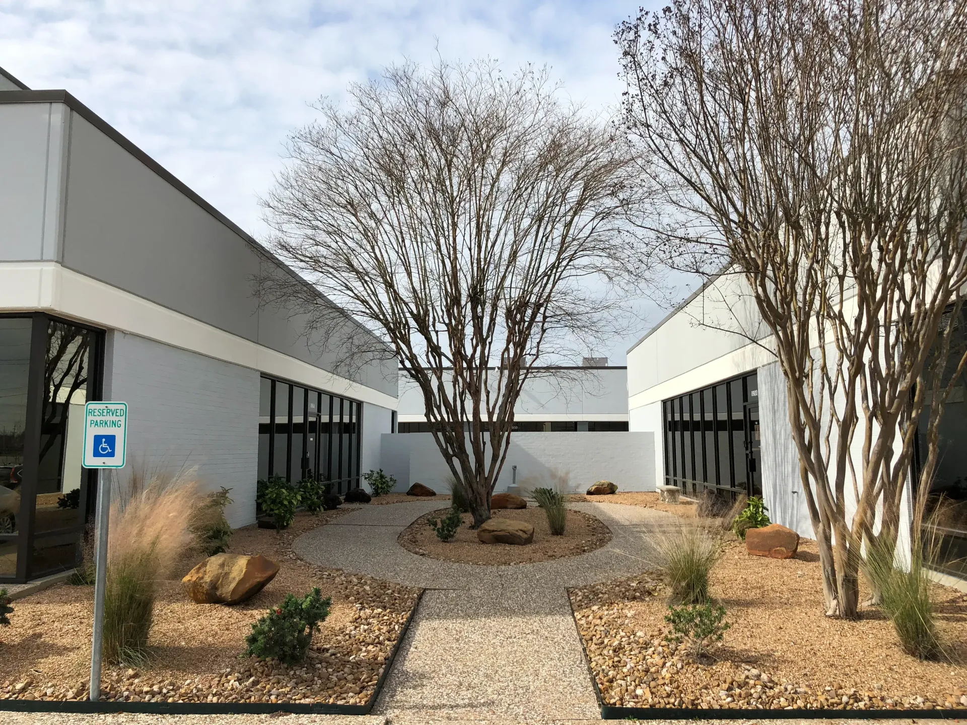 Modern office courtyard with gravel path, trees, and low gray-and-white buildings