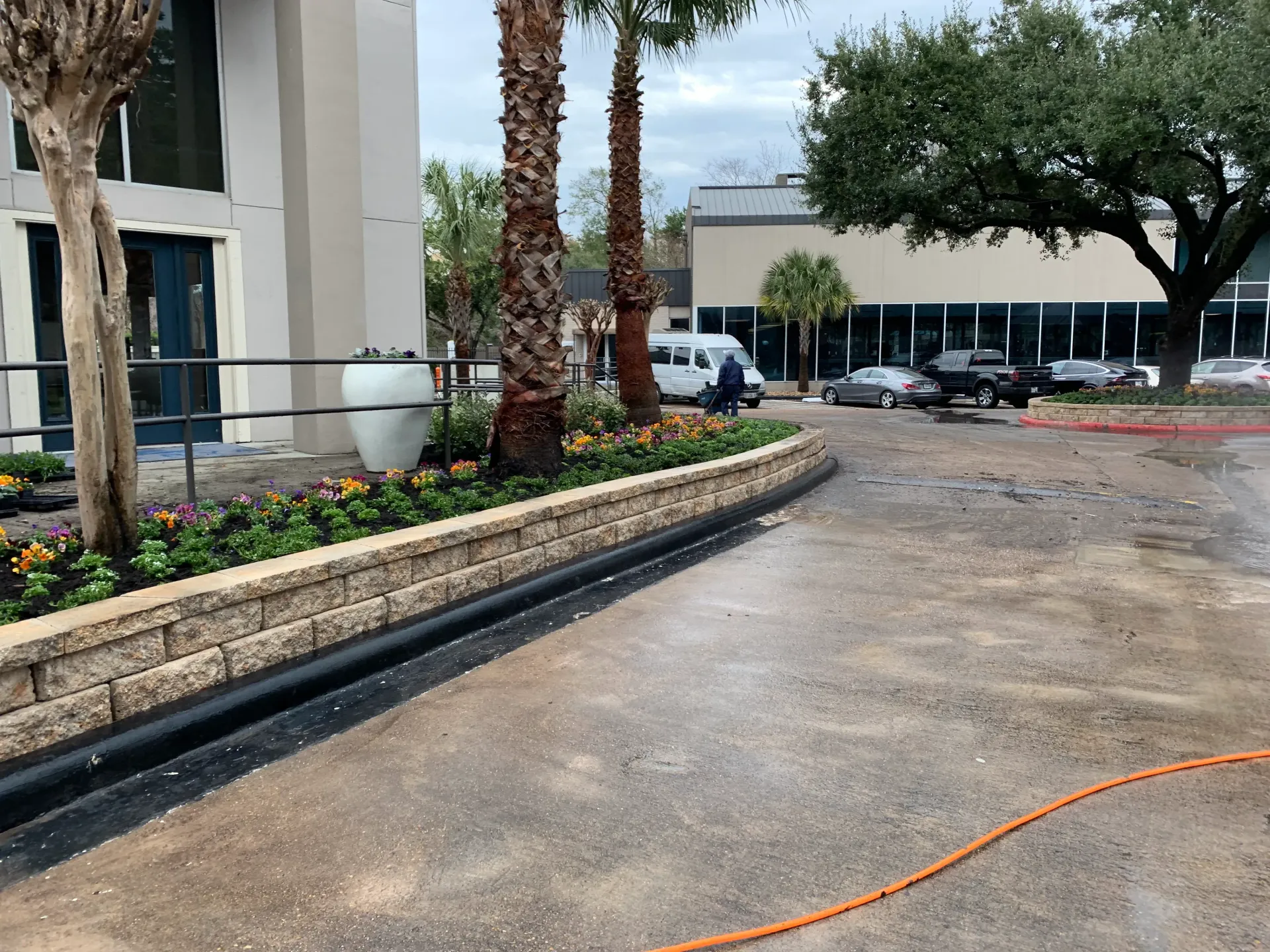 Construction site with gravel driveway, planter beds, palm trees, and parked cars near a building