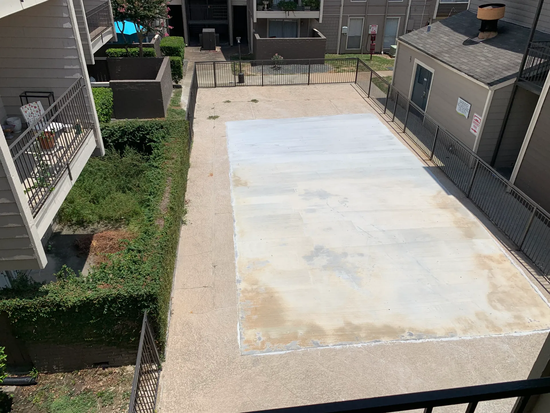 Empty concrete patio area between apartment buildings, bordered by gravel and shrubs.