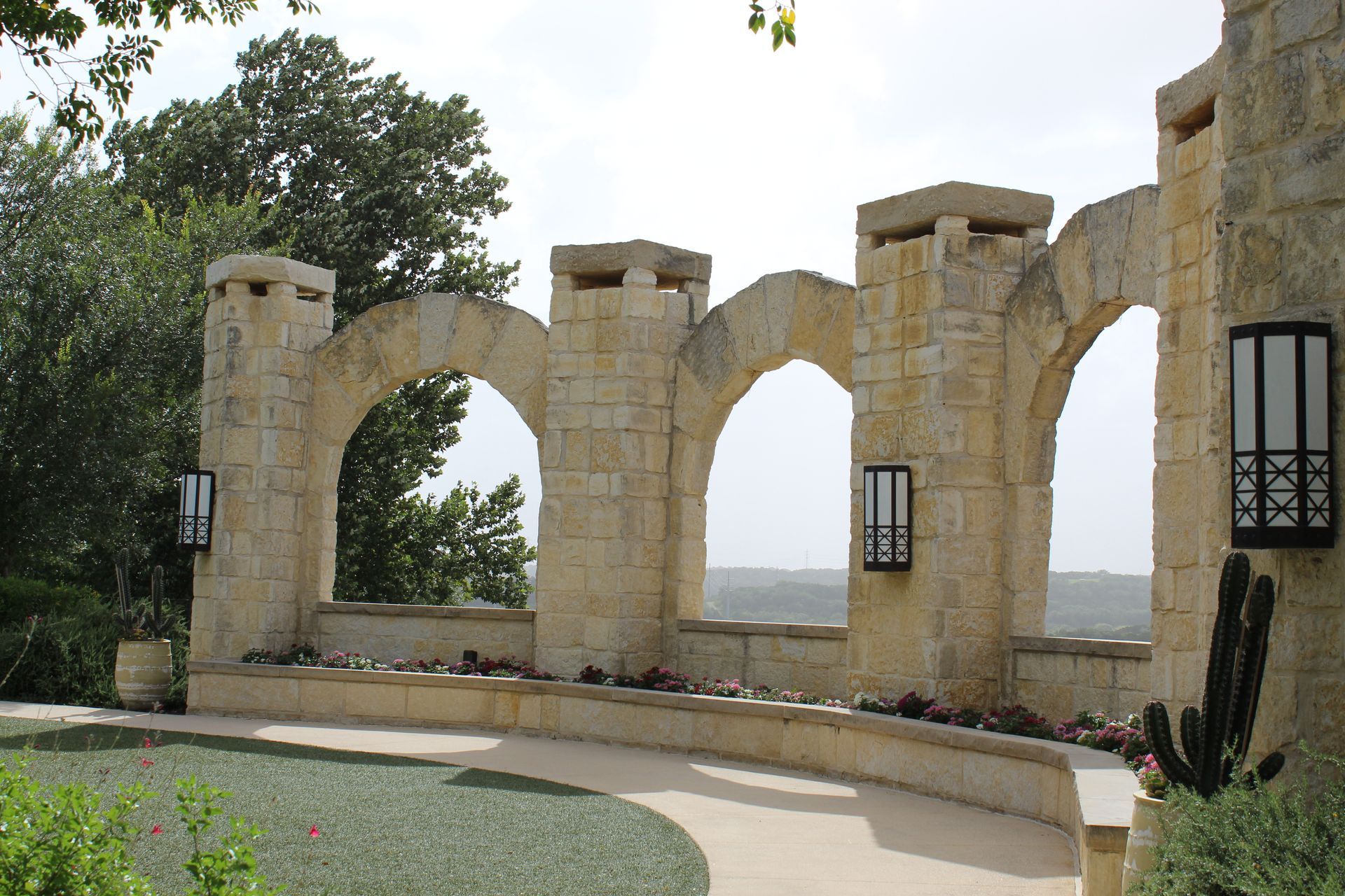 Stone archways and lanterns in a landscaped courtyard with trees and a distant view beyond the walls