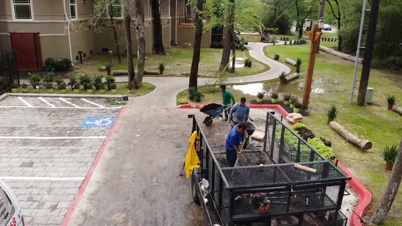 Workers loading a truck in a wet apartment parking lot with trees and buildings nearby