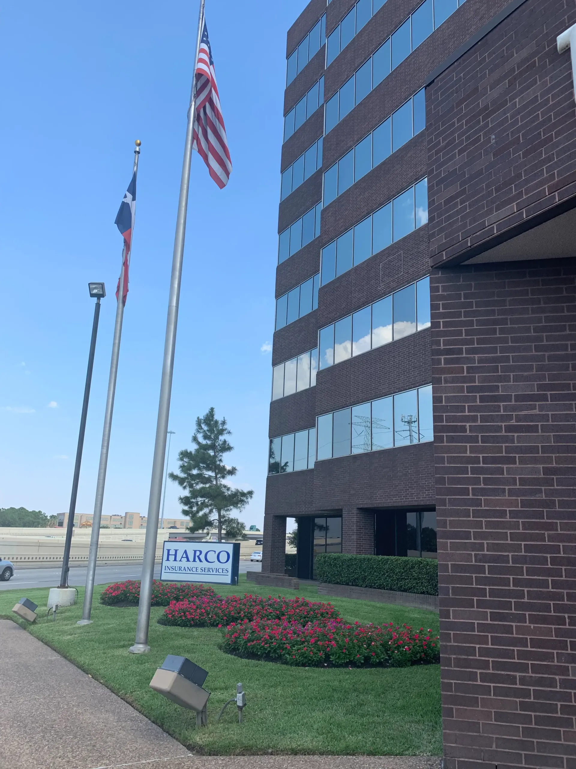 Office building with American flags, flower bed, and sidewalk under a blue sky