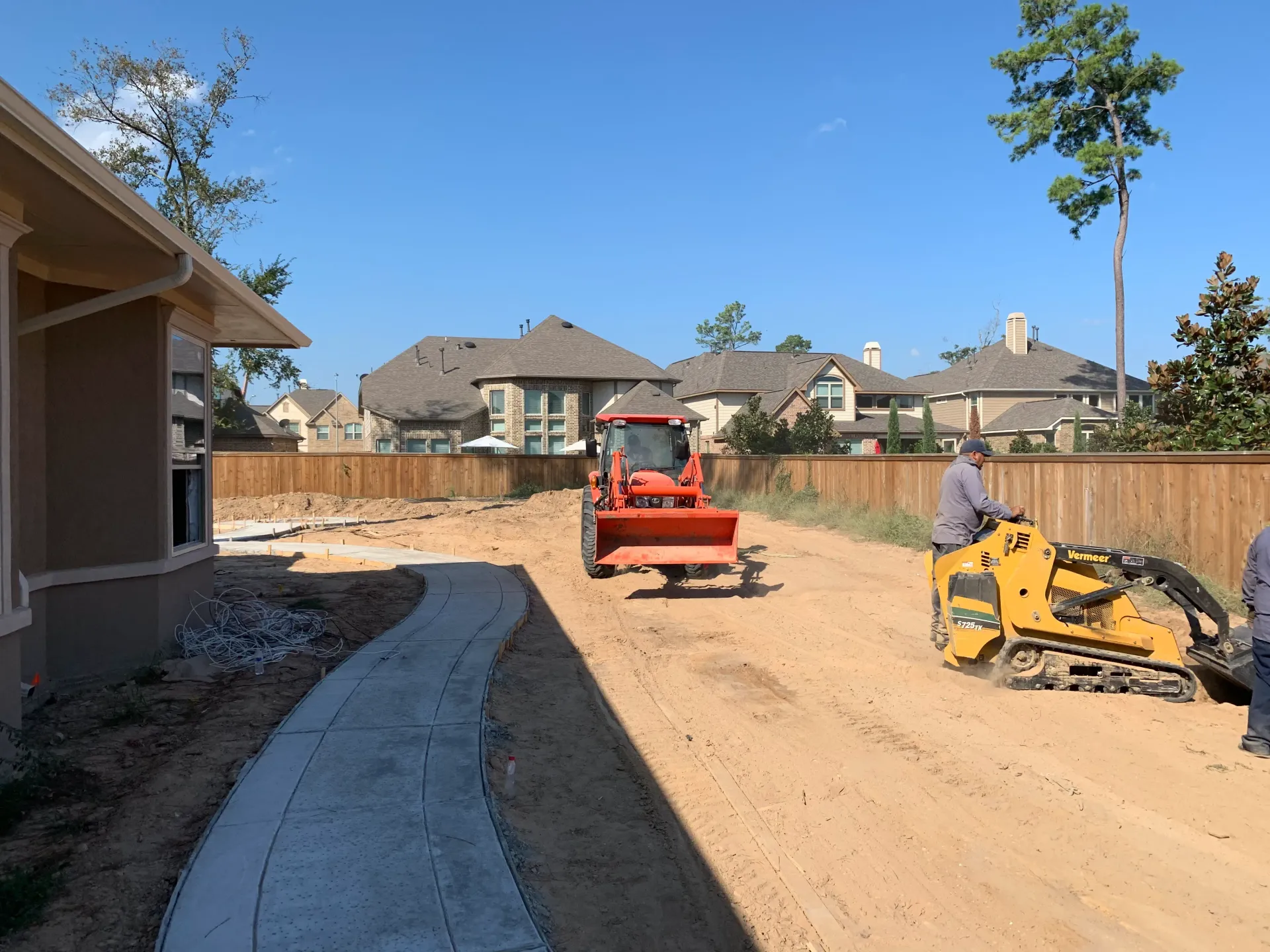 Construction site with red dumper and yellow excavator on a dirt lot beside houses