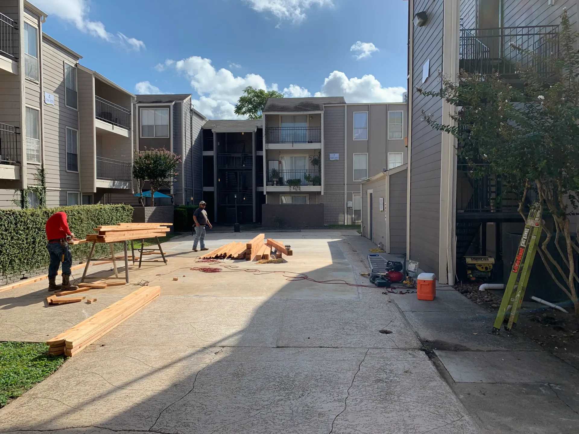 Apartment courtyard under construction with gravel path, benches, workers, and tall buildings.