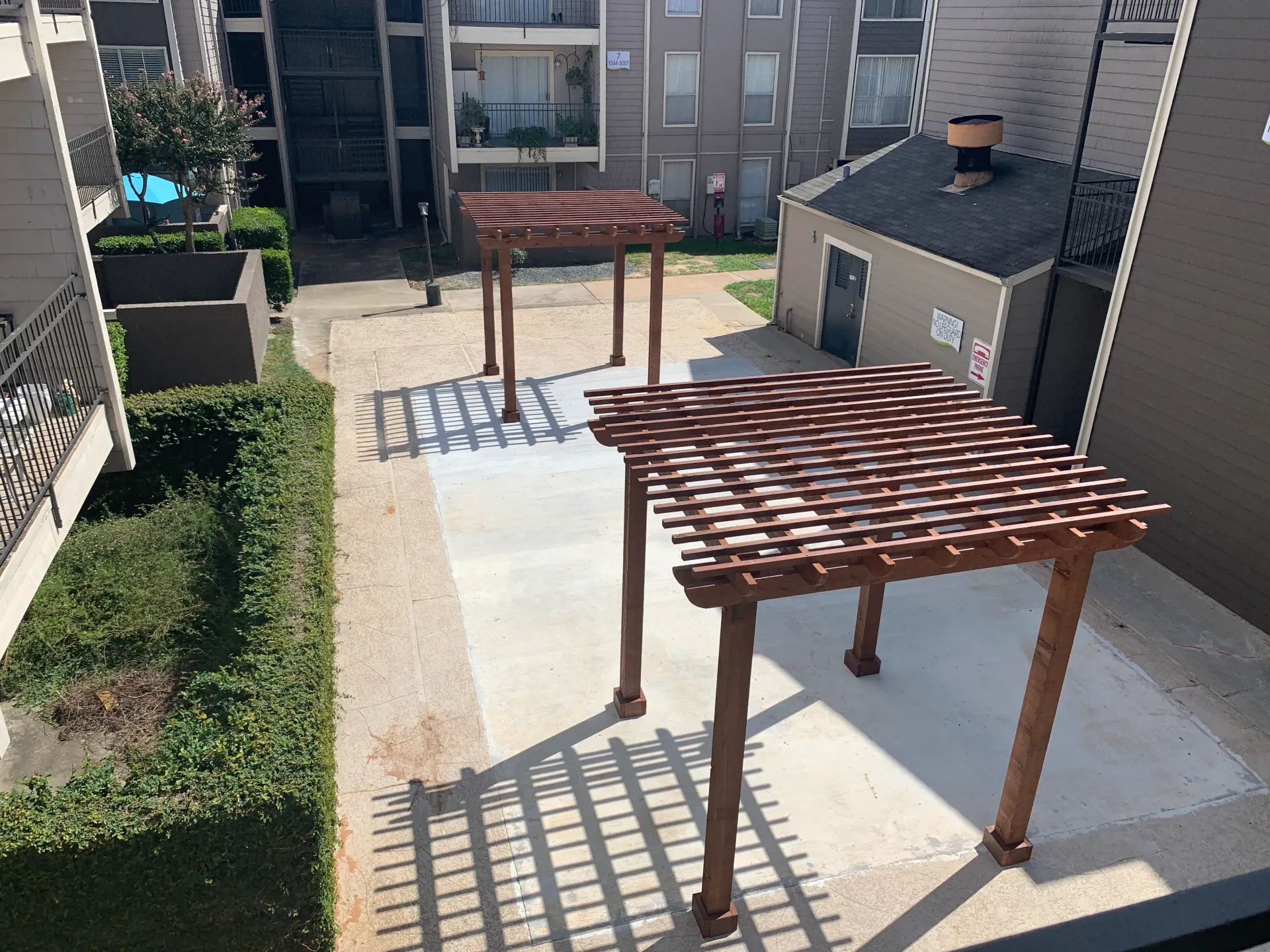Rooftop patio with wooden pergolas casting shadows between apartment buildings.