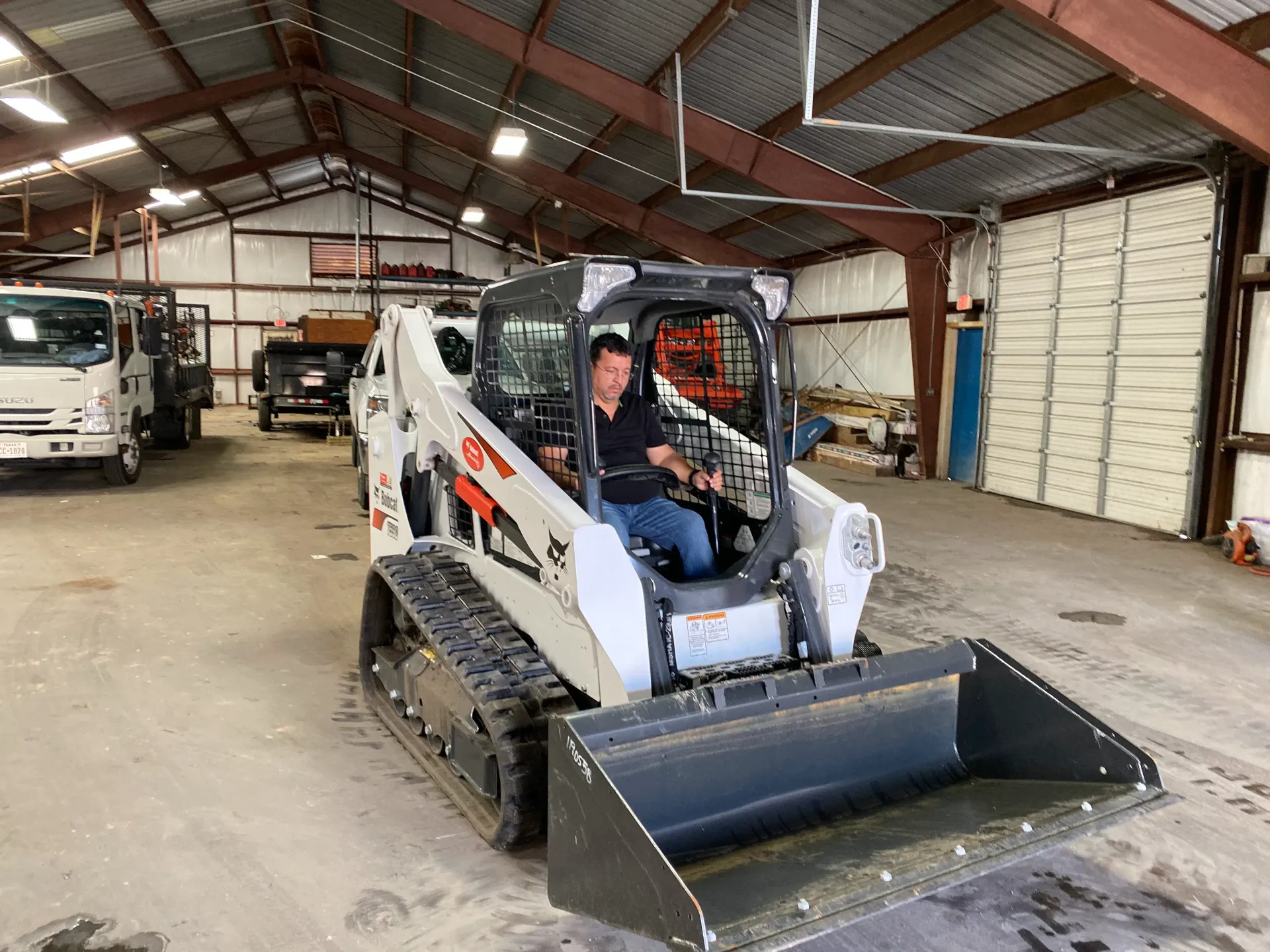 Person driving a white skid-steer loader with bucket inside a warehouse