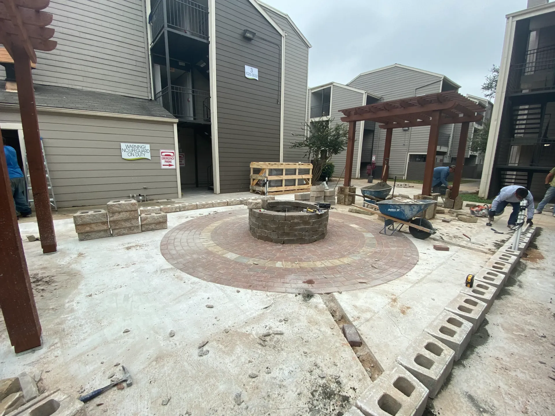 Outdoor construction site with a circular stone patio, workers, and building materials beside a house