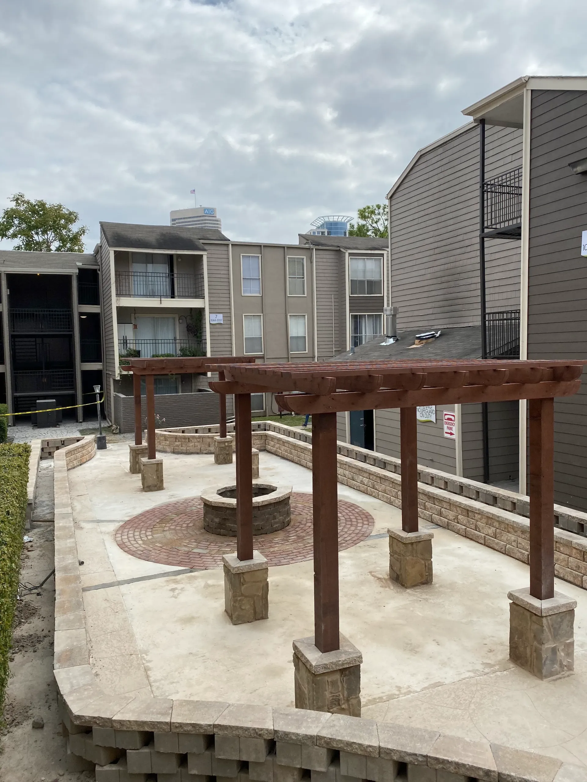 Outdoor apartment courtyard with a raised wooden pergola and concrete planters under a cloudy sky