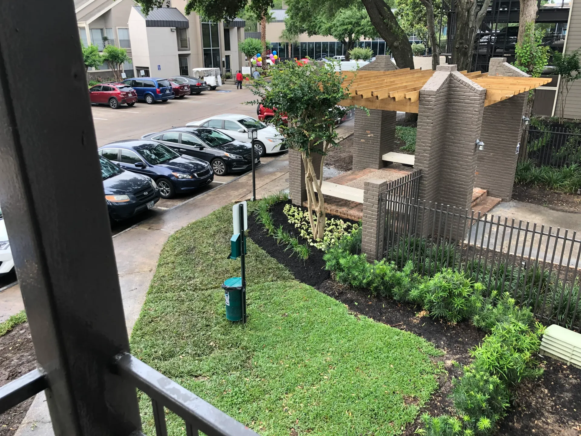 Apartment courtyard with parked cars, green lawn, and a small gazebo-like structure.