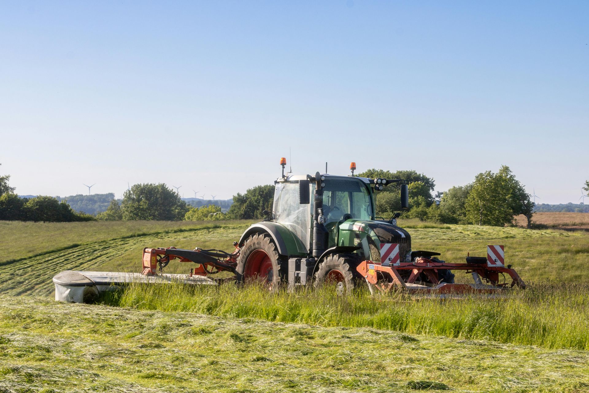 Tractor mowing grass in a sunny field with open farmland in the background