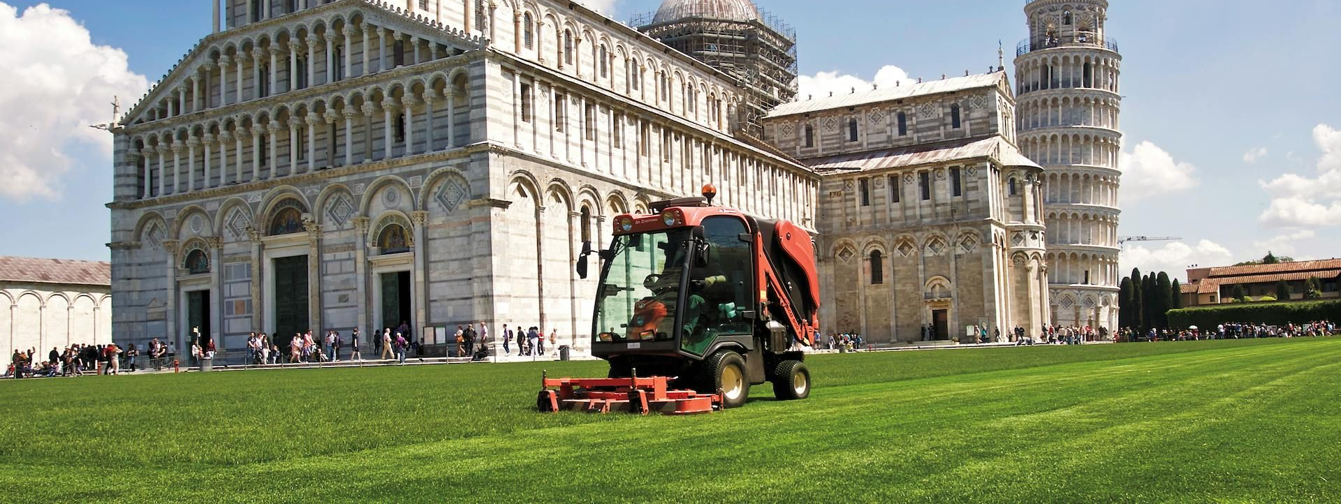 Lawn mower trimming grass in front of the Leaning Tower of Pisa and cathedral