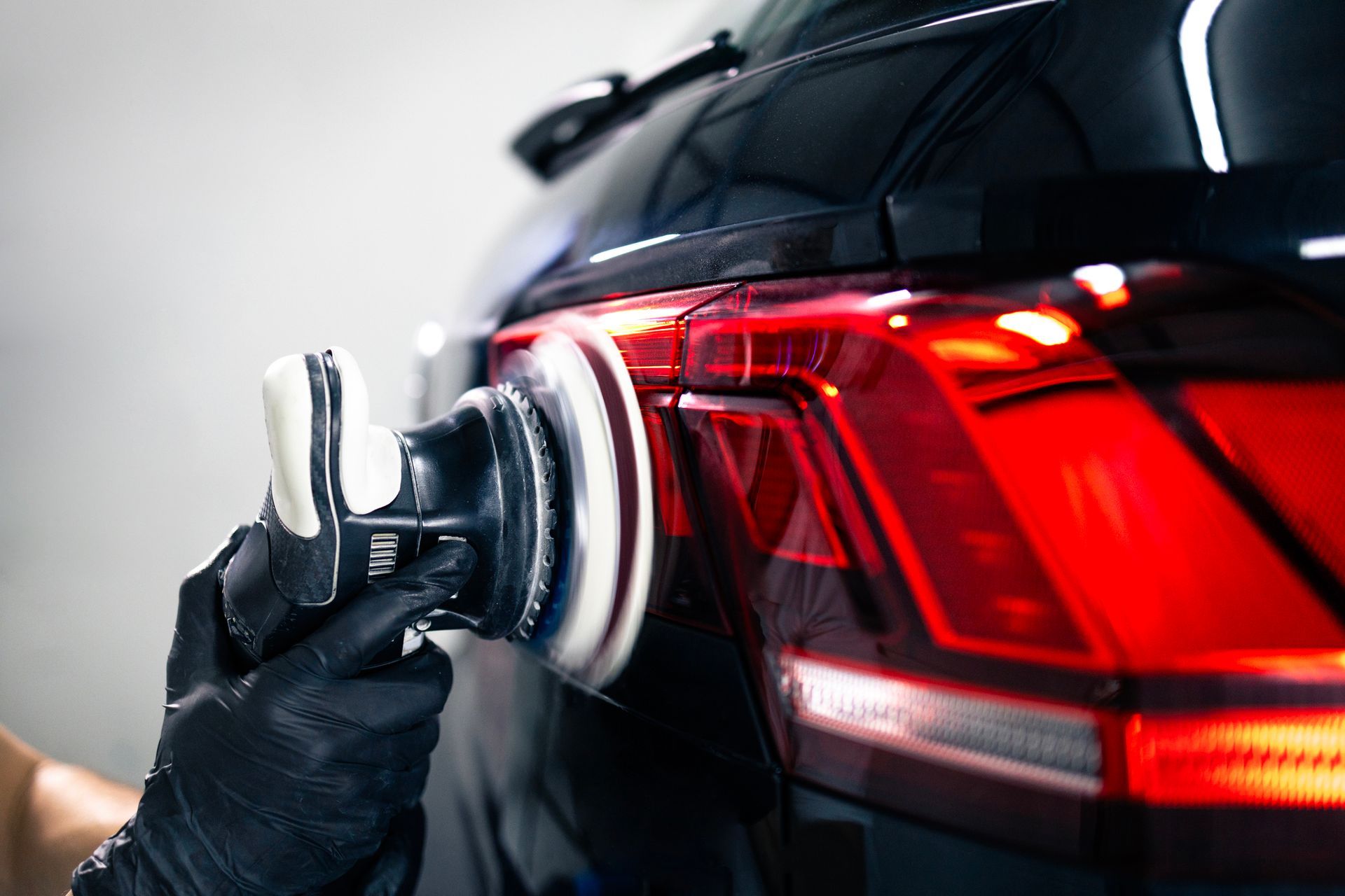Una persona lucida il fanale posteriore di un'auto nera con una lucidatrice rotativa.