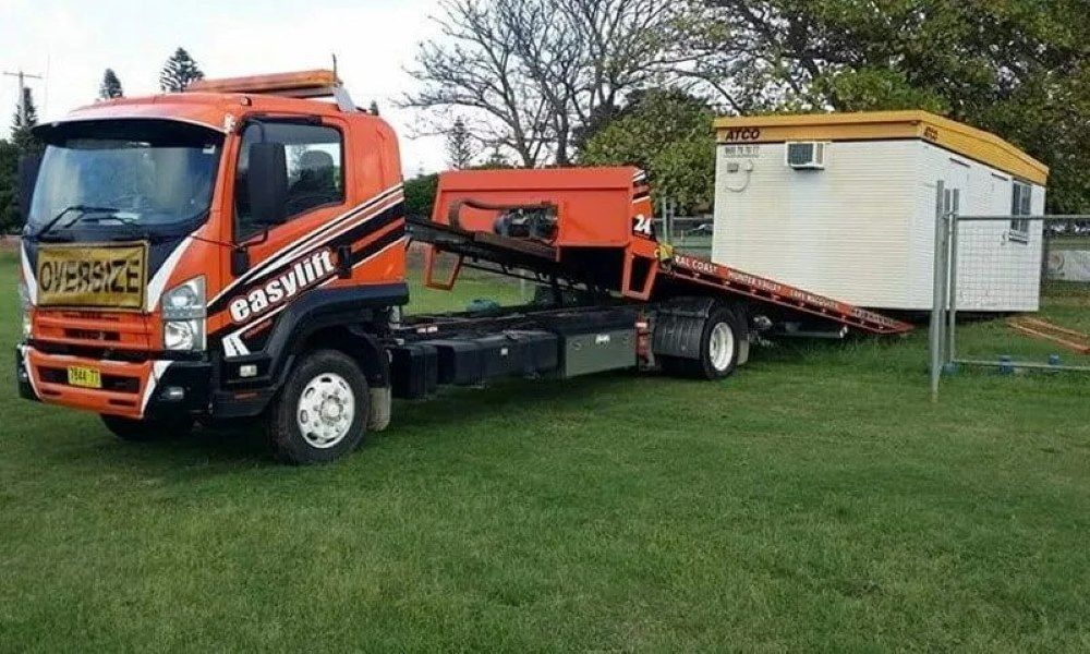 An Orange Tow Truck Is Parked in A Grassy Field — Easylift Towing NSW Pty Ltd In Beresfield, QLD