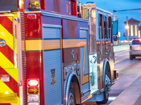 A side view of a red and blue fire engine parked on a bridge during twilight, with a car visible in the distance.
