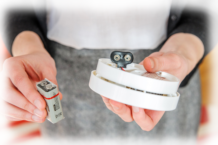 A person holding a smoke alarm and a 9V battery, preparing to install or replace the battery.