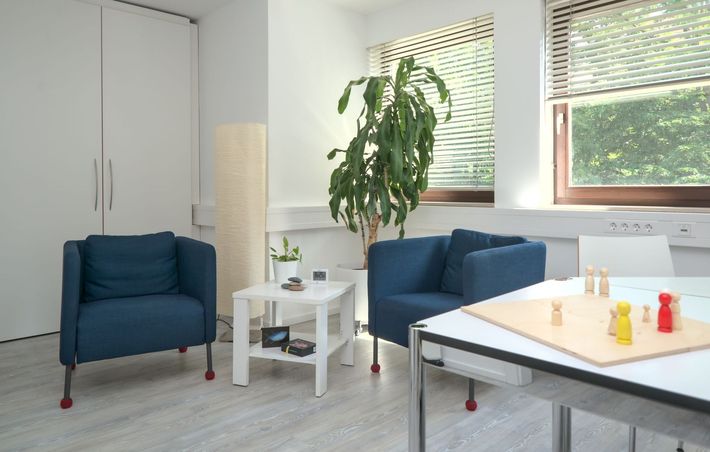 Sprechzimmer: blauer Sessel, Spielbrett mit Holzfiguren in holzfarben, gelb und rot