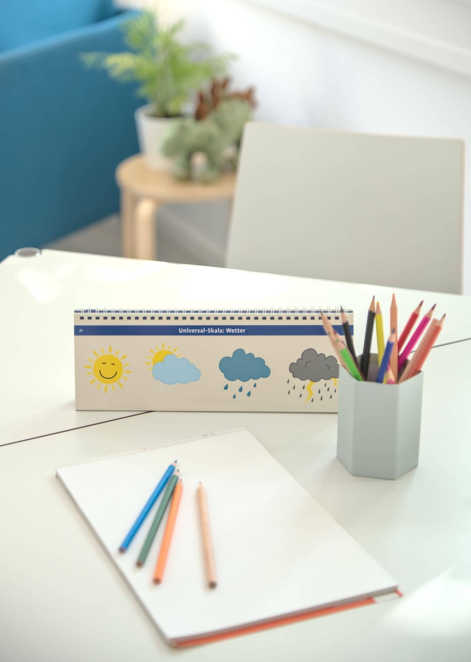 Sprechzimmer, Tisch mit einem Malblock und Buntstiften und Wettersymbolen.