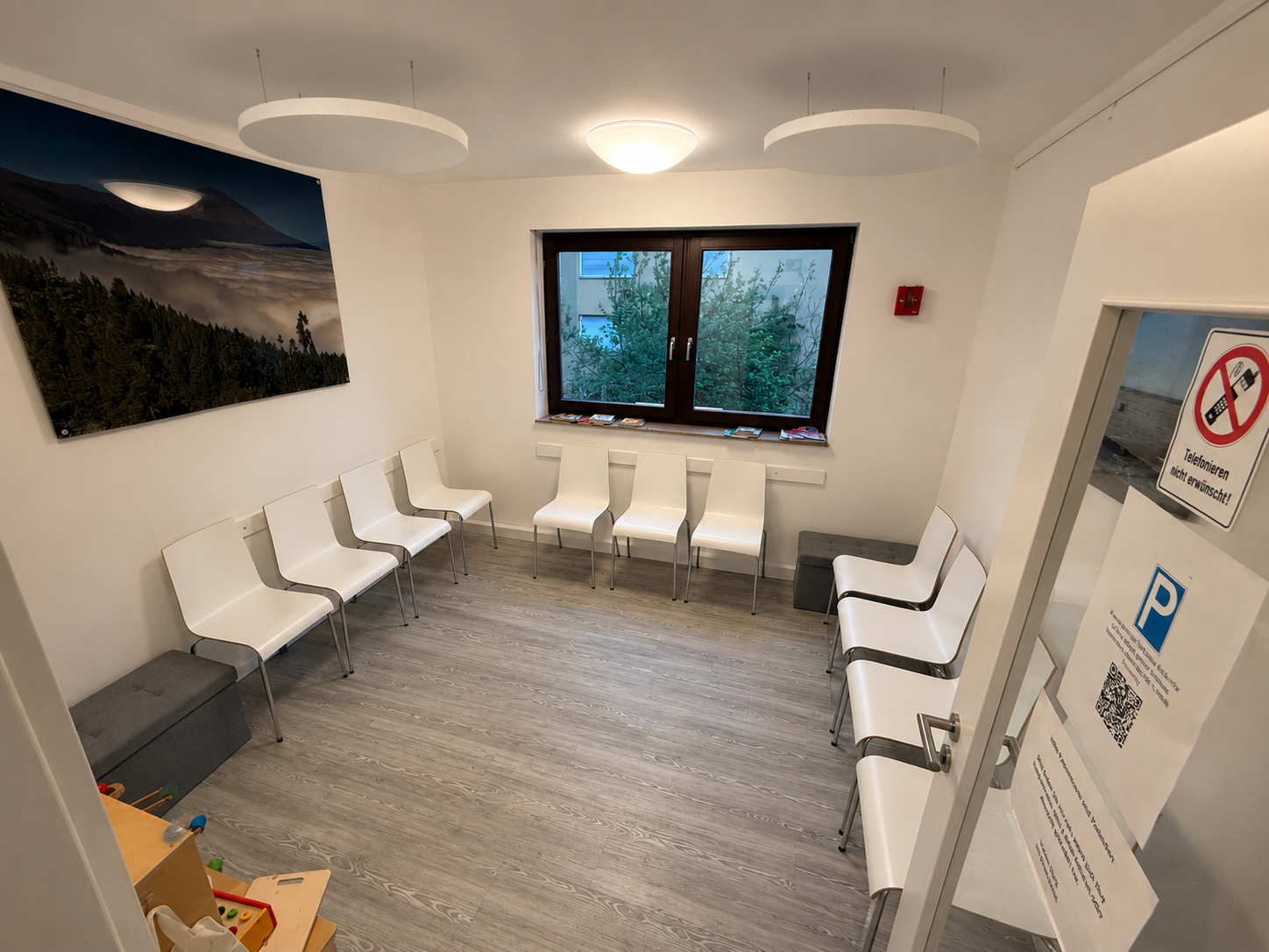 Wartezimmer mit weißen Stühlen und Bildern an der Wand