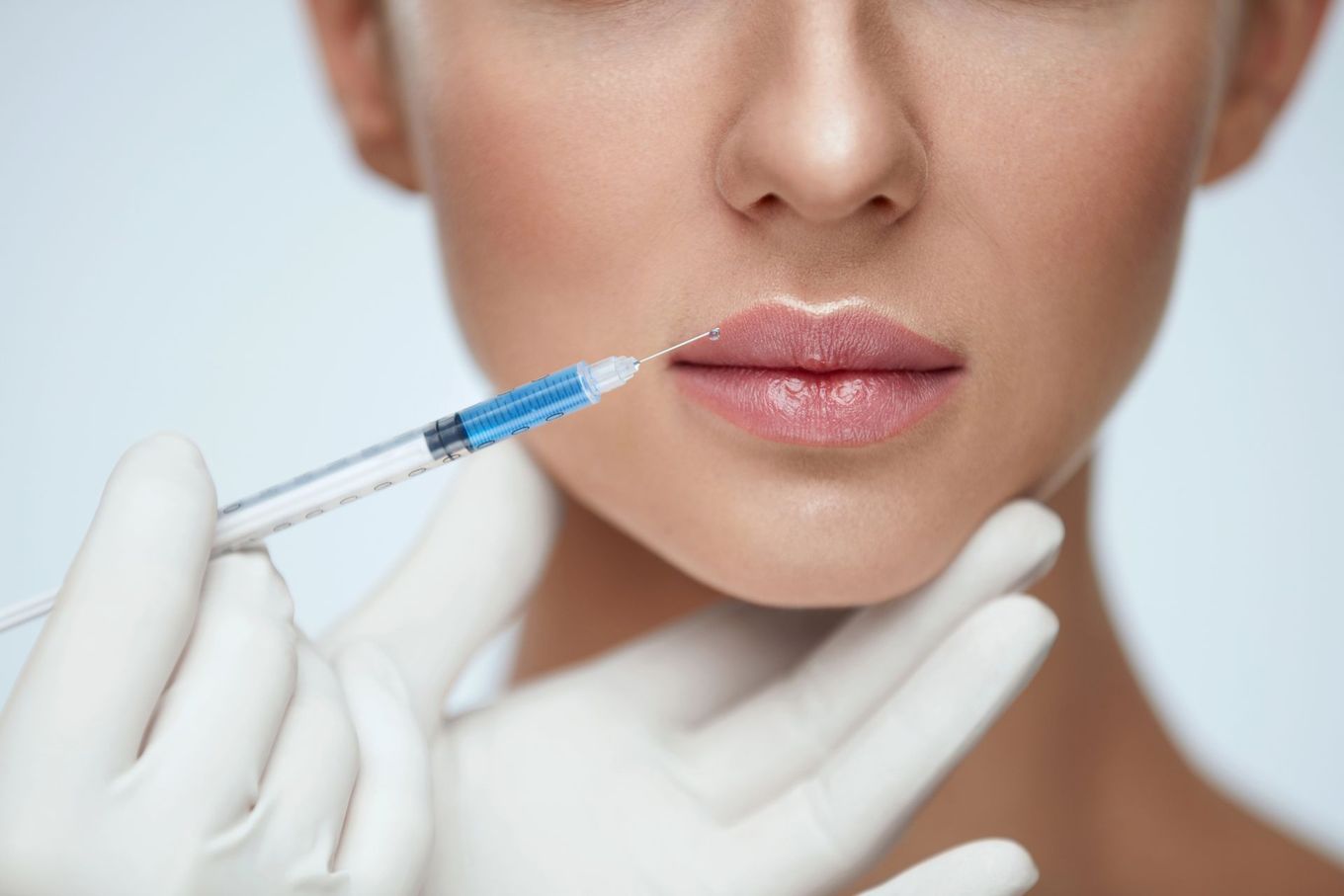En un entorno clínico, manos enguantadas inyectan relleno en los labios de una persona con una jeringa.