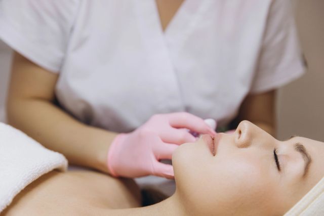 Una terapeuta de spa le da un masaje en la cara a una clienta con una toalla blanca debajo de la barbilla.