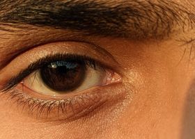 Primer plano de un ojo marrón con pestañas oscuras y piel de tono cálido.