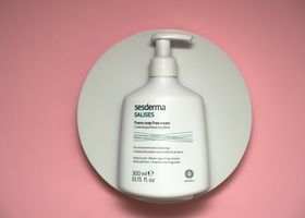 Frasco de loción corporal Sesderma sobre una bandeja redonda blanca con fondo rosa.