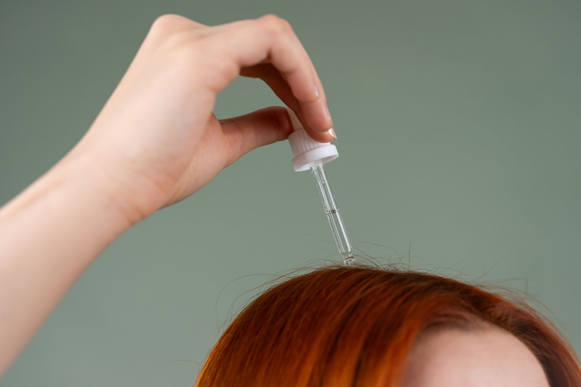 Aplicación manual de gotas líquidas sobre cabello rojo con un frasco cuentagotas