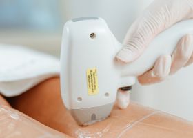 Un médico con guantes utiliza una sonda de ultrasonido manual en el abdomen de un paciente.