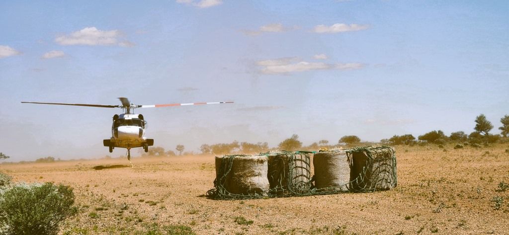 Helicopter hovering over a dry field with stacked hay bales under a blue sky