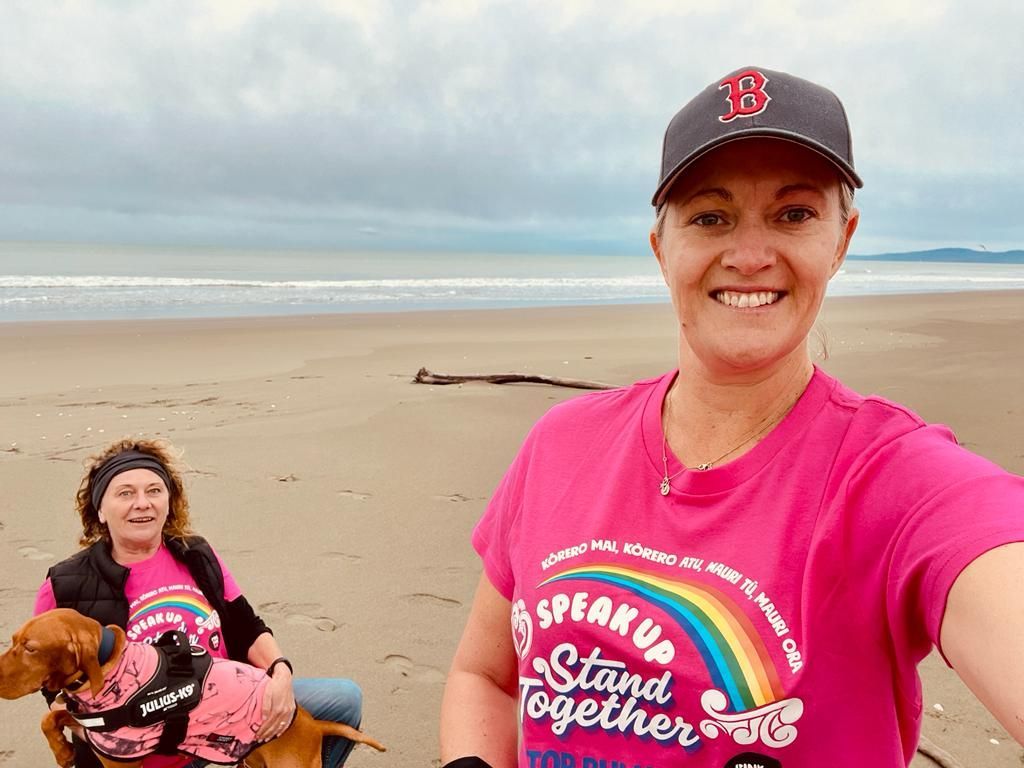 A woman in a pink shirt is standing on a beach with two dogs.