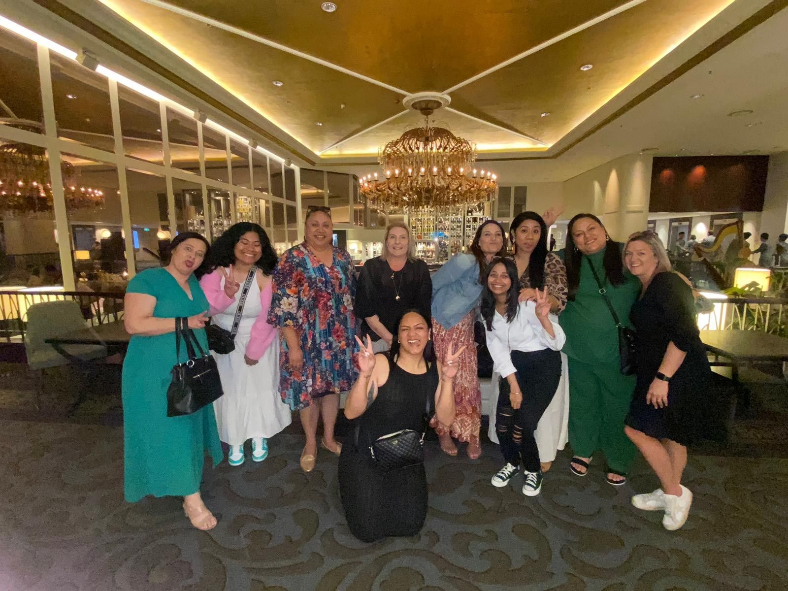 A group of women are posing for a picture in a room with a chandelier.