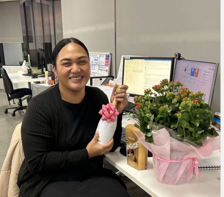 A woman is sitting at a desk holding a vase of flowers.