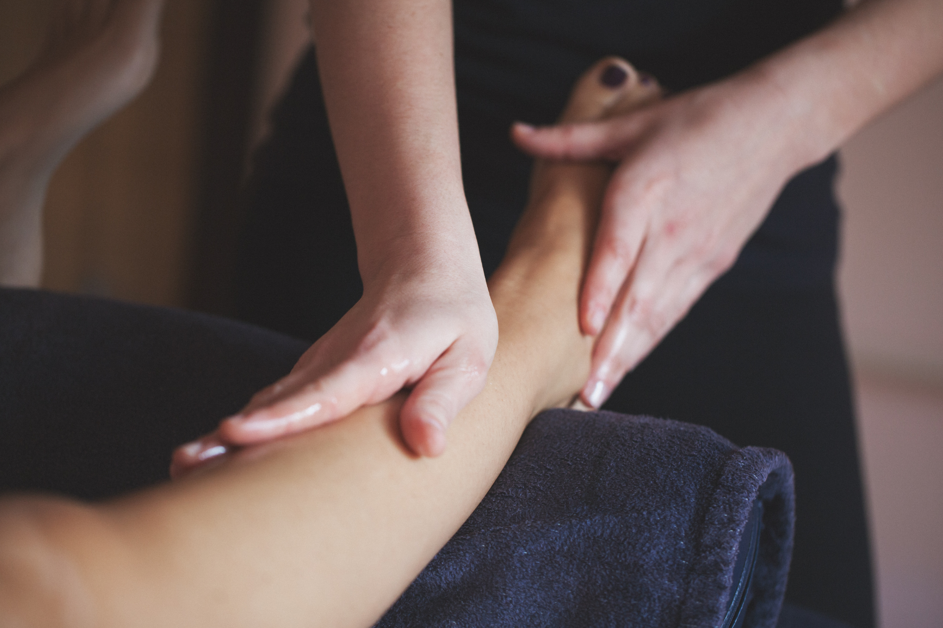 Two hands giving a massage to a leg on a dark towel